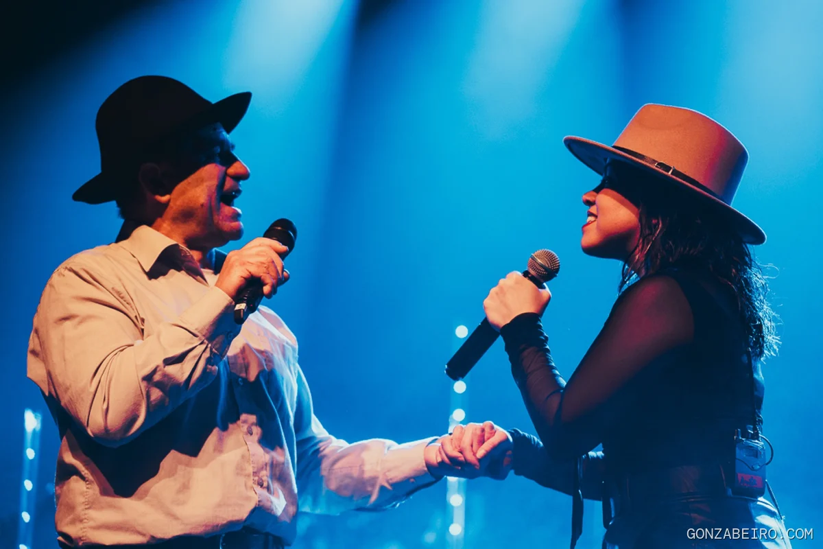 Anita Valiente y otro músico cantan frente a frente bajo luces azules.